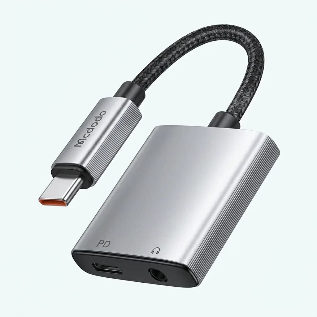 Mcdodo silver USB-C audio adapter with braided black cable, USB-C male connector, 3.5mm headphone jack and USB-C PD charging port on a white background.